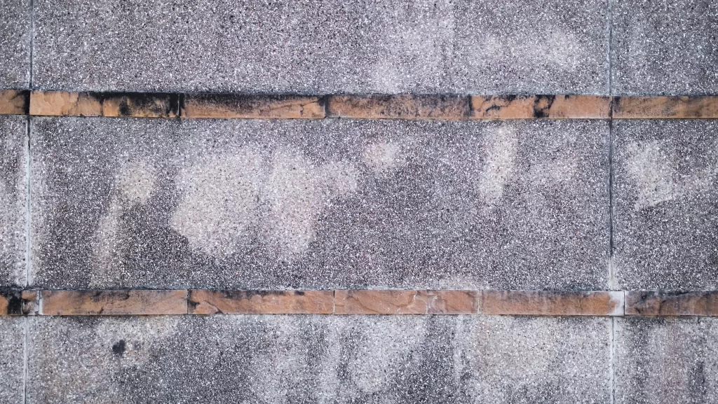 Close-up of weathered concrete surface with two horizontal brown lines and discoloration.