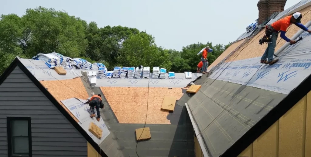 3 roofers with orange shirts on a roof.