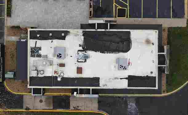 Aerial view of a rectangular flat roof building with rooftop equipment and adjacent parking areas.