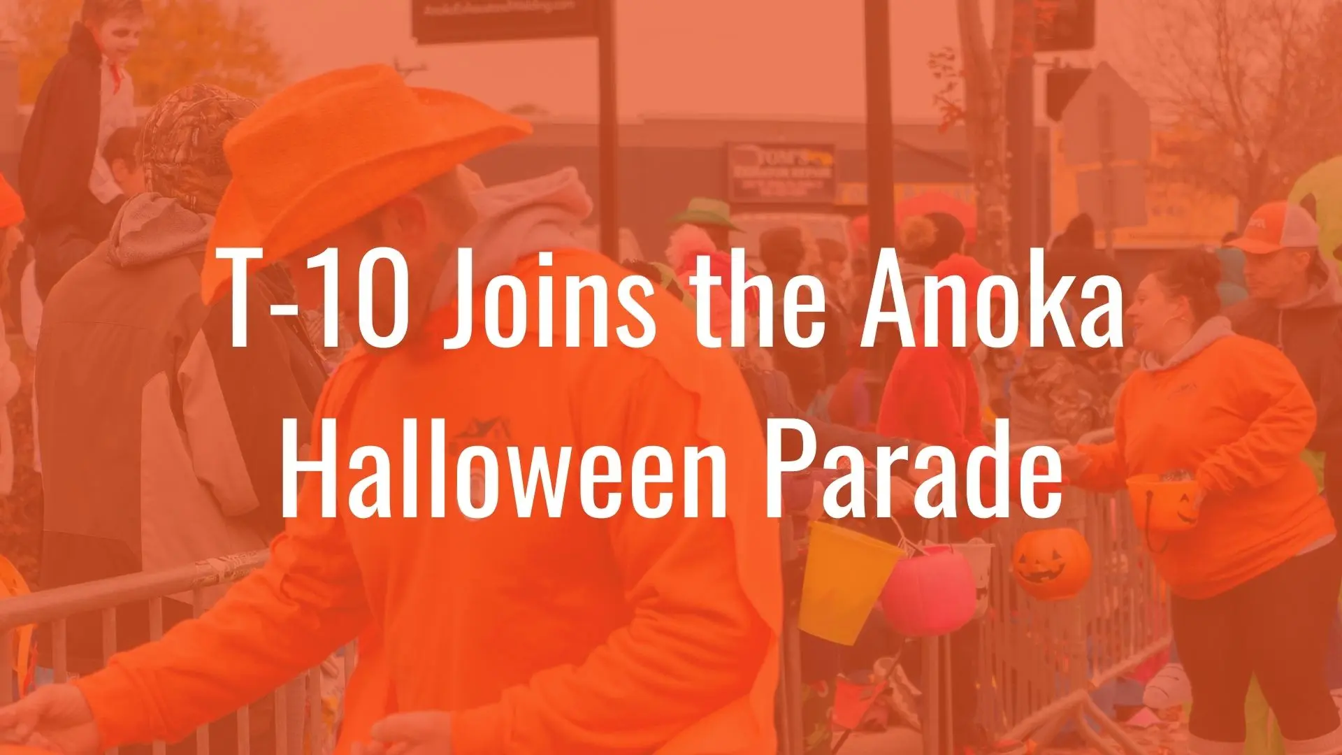 People in orange clothing with candy containers at the Anoka Halloween Parade event.