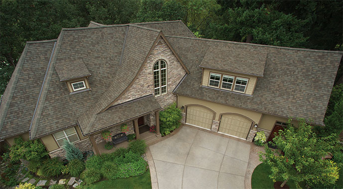 Two-story house with multi-gabled roof, stone and siding exterior, two-car garage, front porch, and surrounding greenery.