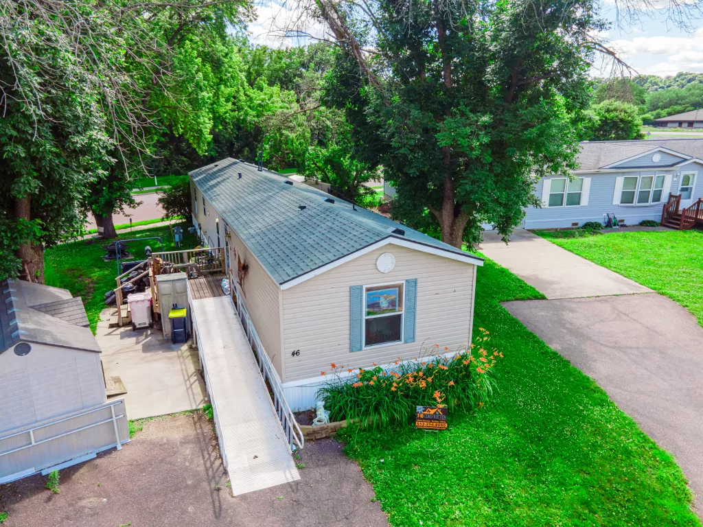 Beige single-story mobile home with blue shutters, ramp entrance, shed, and construction sign.