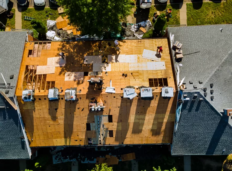 Aerial view of workers installing plywood sheets on a residential roof during replacement.