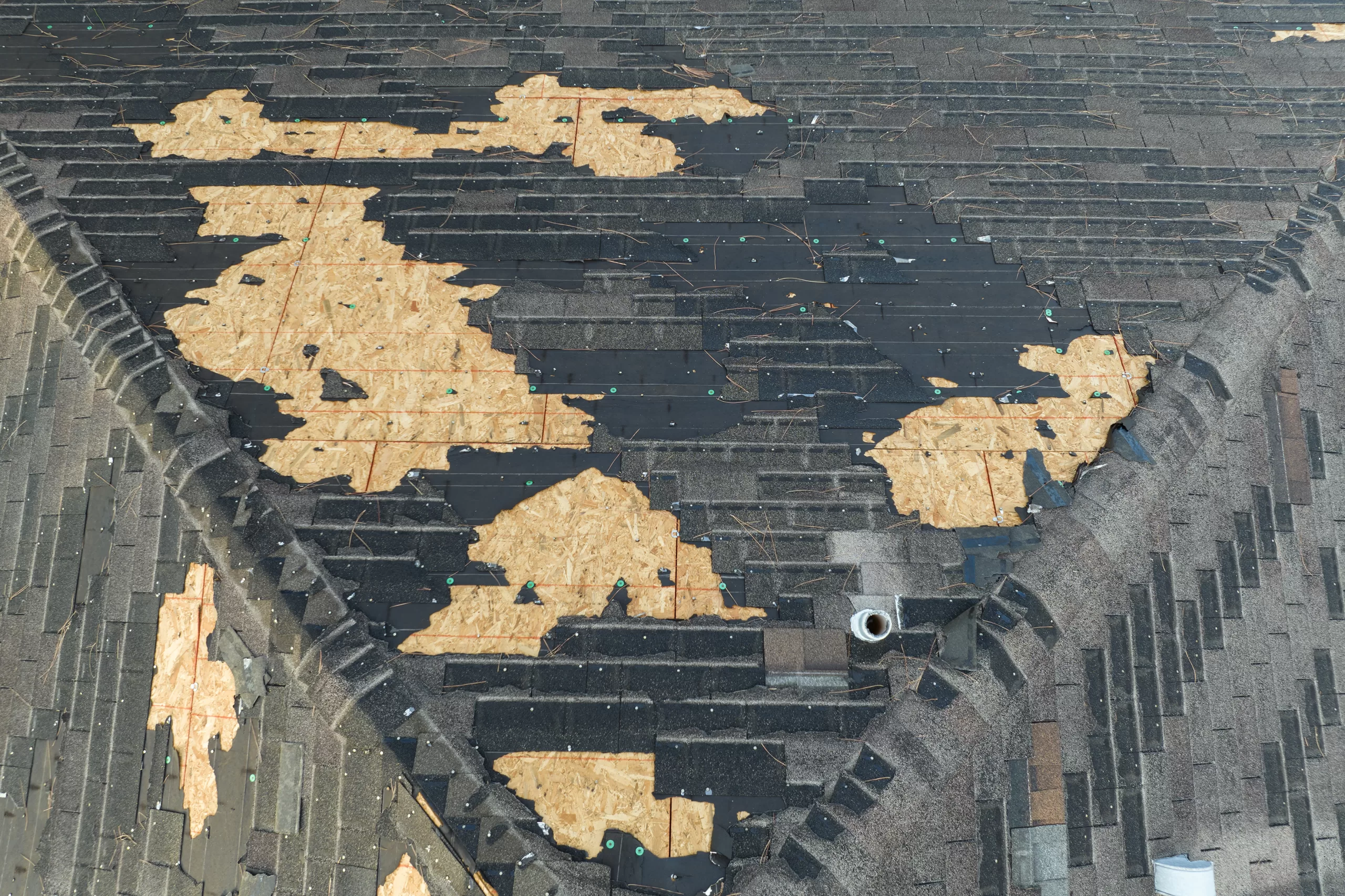 Roof with missing and damaged shingles exposing wooden sheathing and scattered nails.