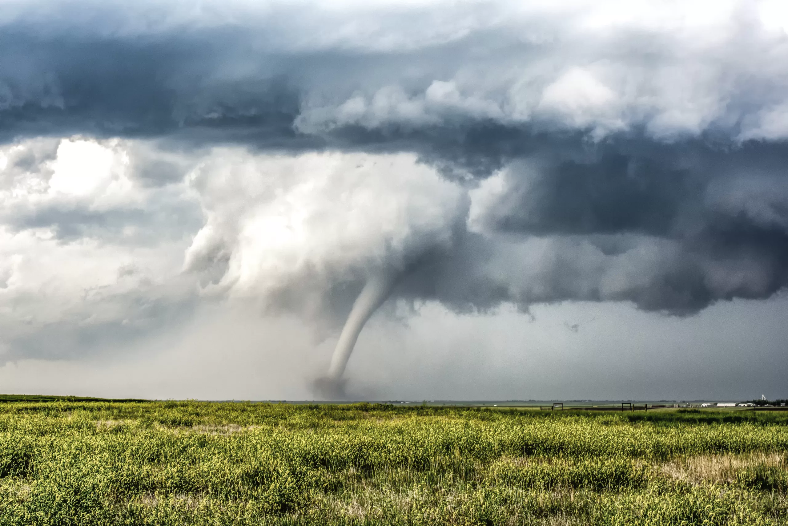 Tornado touching down over a flat grassy field under dark storm clouds.